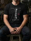 "A model wearing a black scripture-based t-shirt in a mechanical workshop setting. The industrial graphic visualizes catastrophic mechanical failure to represent the importance of following God's Word, creating a conversation-starting urban aesthetic."