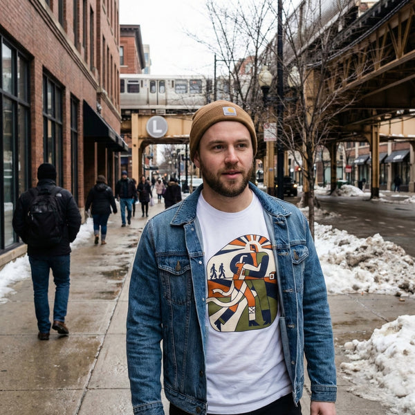 Man wearing a denim jacket and graphic t-shirt on a city street with snow and pedestrians.