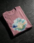 Heather Orchid Thorn Tee folded on dark stone, showing a glowing cracked vessel, vines, flowers and wings.