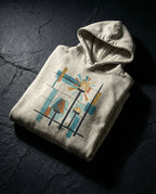 Oatmeal Heather Bushel Hoodie folded on dark stone, showing geometric lamps, teal and gold rays, colored blocks and a black grid.