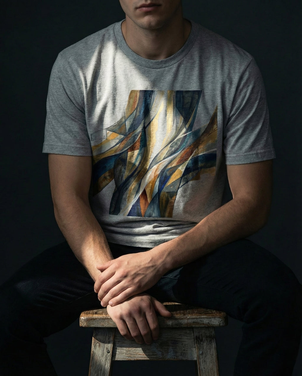 "Selah Supply Co. The Imputed Tee in athletic heather gray. Model sitting on a wooden stool in a technical workshop wearing a graphic tee that uses abstract art to represent the doctrine of imputed righteousness from Romans 5:19."