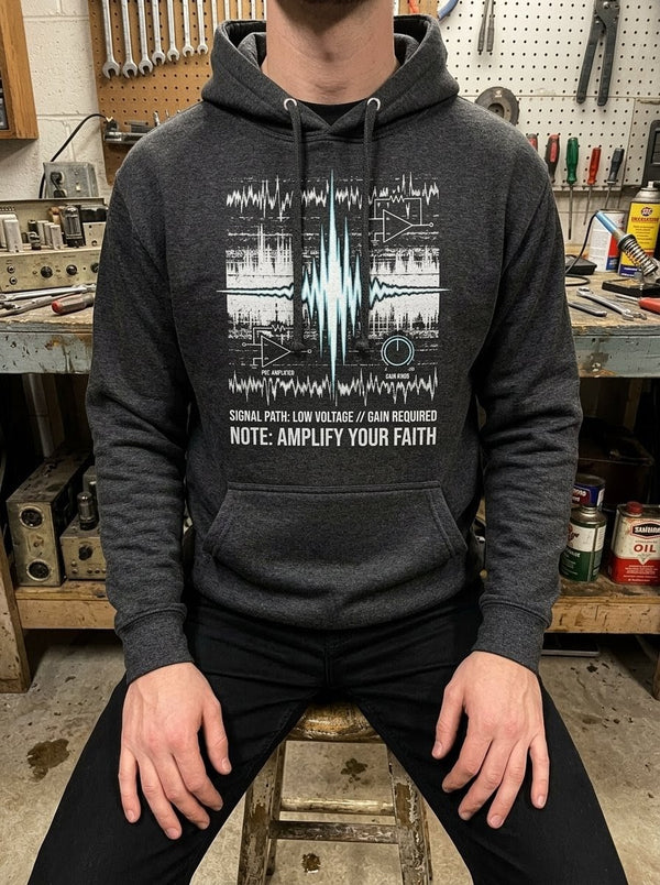 Man in a gritty industrial workshop wearing a Selah Supply Co Charcoal Heather 'Component: Gain' hoodie featuring a high-voltage waveform spike graphic inspired by James 5:16.