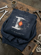 Navy Blazer Yield hoodie folded on a workbench among tools, showing the white I-beam, glowing center and refining-in-progress text.