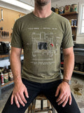 Person in a tool-filled workshop wearing a Selah Supply Co Heather Olive t-shirt with an industrial pressure extraction graphic