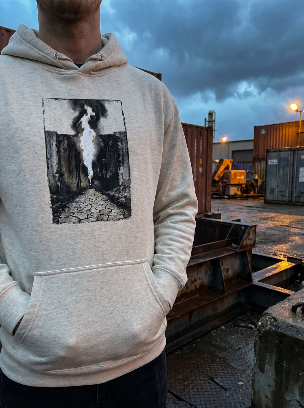  Model wearing the Selah Supply Co. Oatmeal Heather Transmission: Pillar streetwear hoodie in an industrial environment, showcasing the front brutalist graphic artwork.
