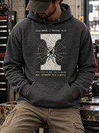 A man wearing a dark heather gray hoodie with a white and gold graphic print on the front, sitting in a workshop environment.