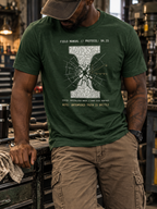 Front view of a standing model in a workshop, wearing a heather emerald T-shirt with a white I-shaped section with a shattered center and radiating fracture lines centered on the front.