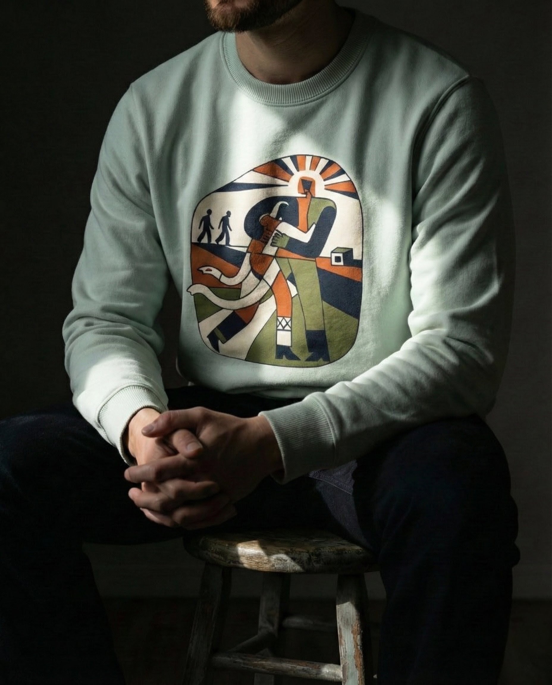 Person wearing a light green sweatshirt with a colorful graphic design sitting on a stool.