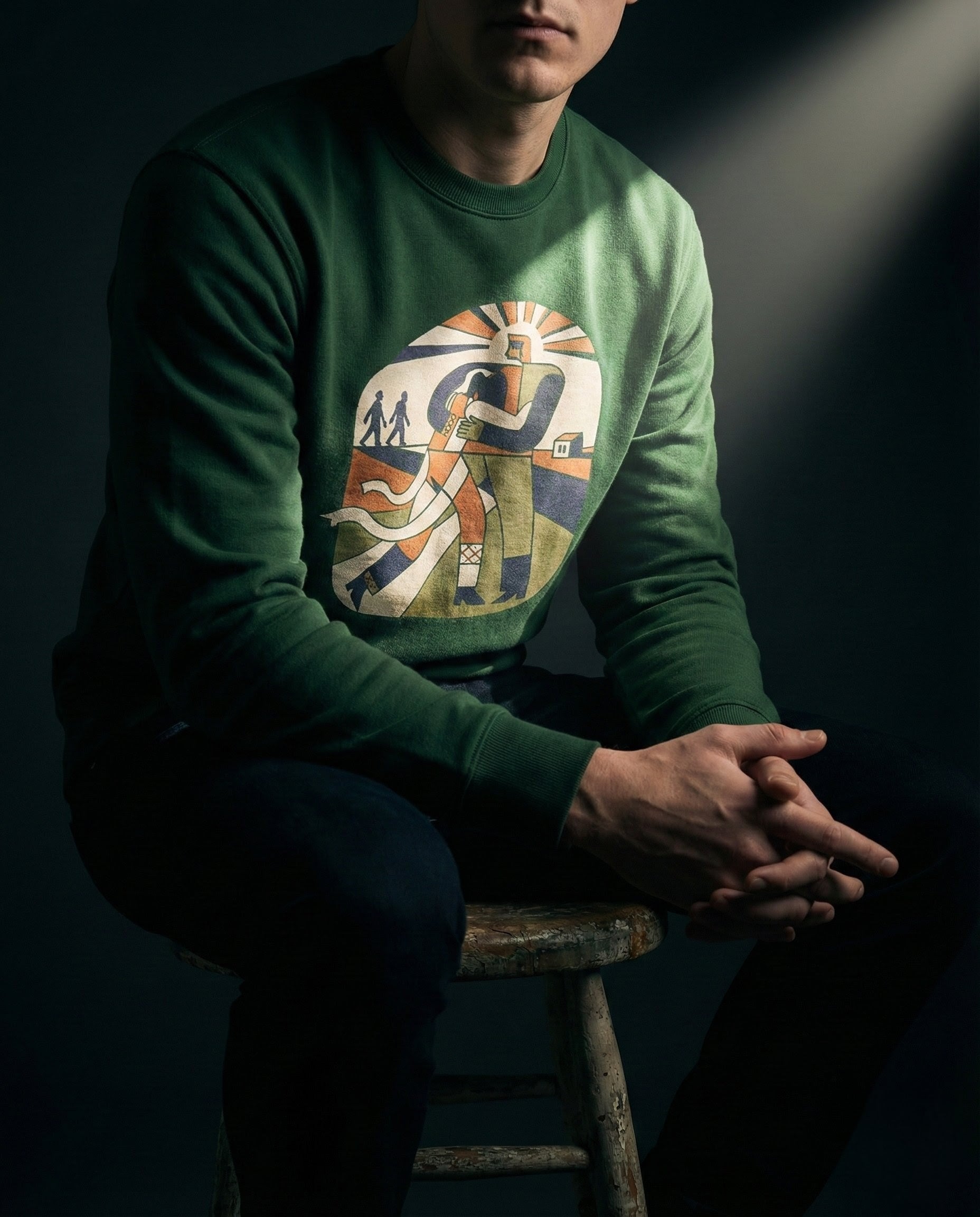Person wearing a green sweater with a graphic design, sitting on a stool against a dark background