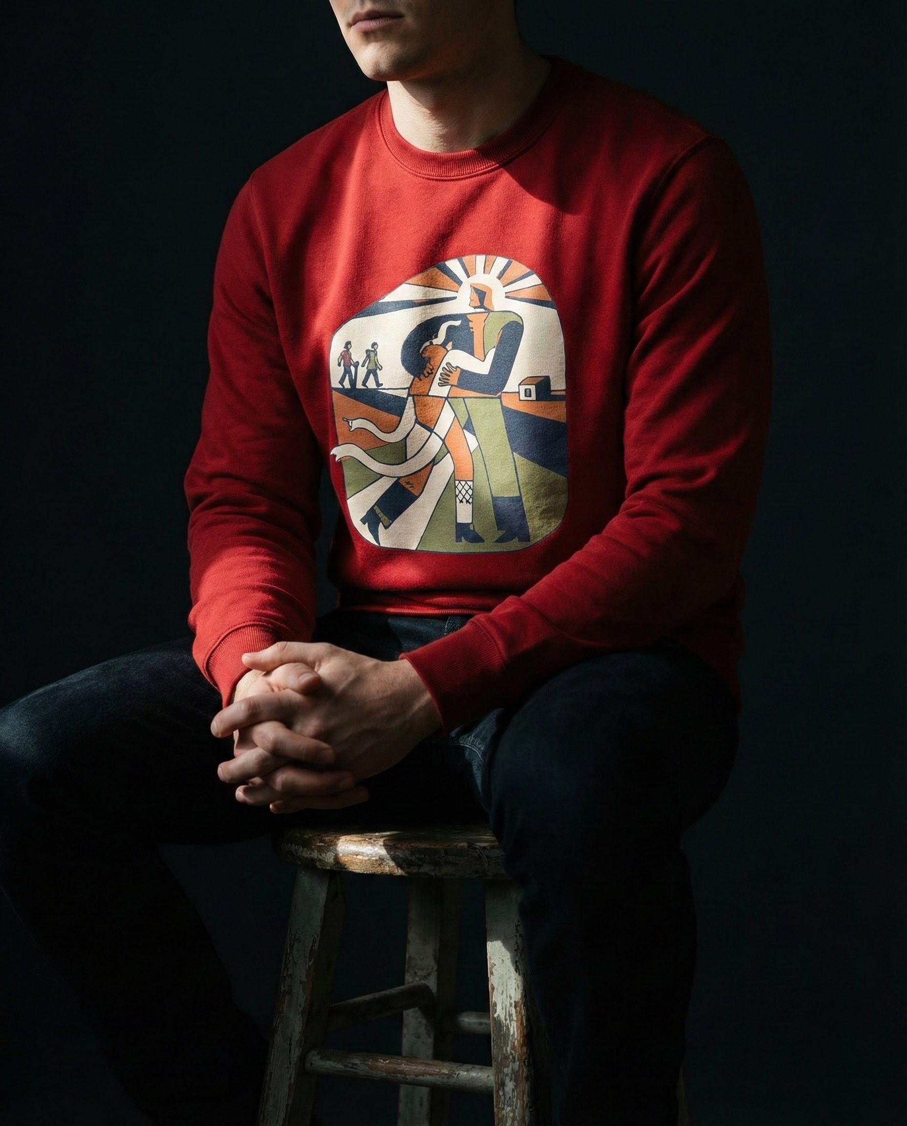 Person wearing a red sweatshirt with a colorful graphic design sitting on a stool against a dark background