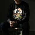 Person wearing a black sweatshirt with a colorful graphic design sitting on a stool against a dark background