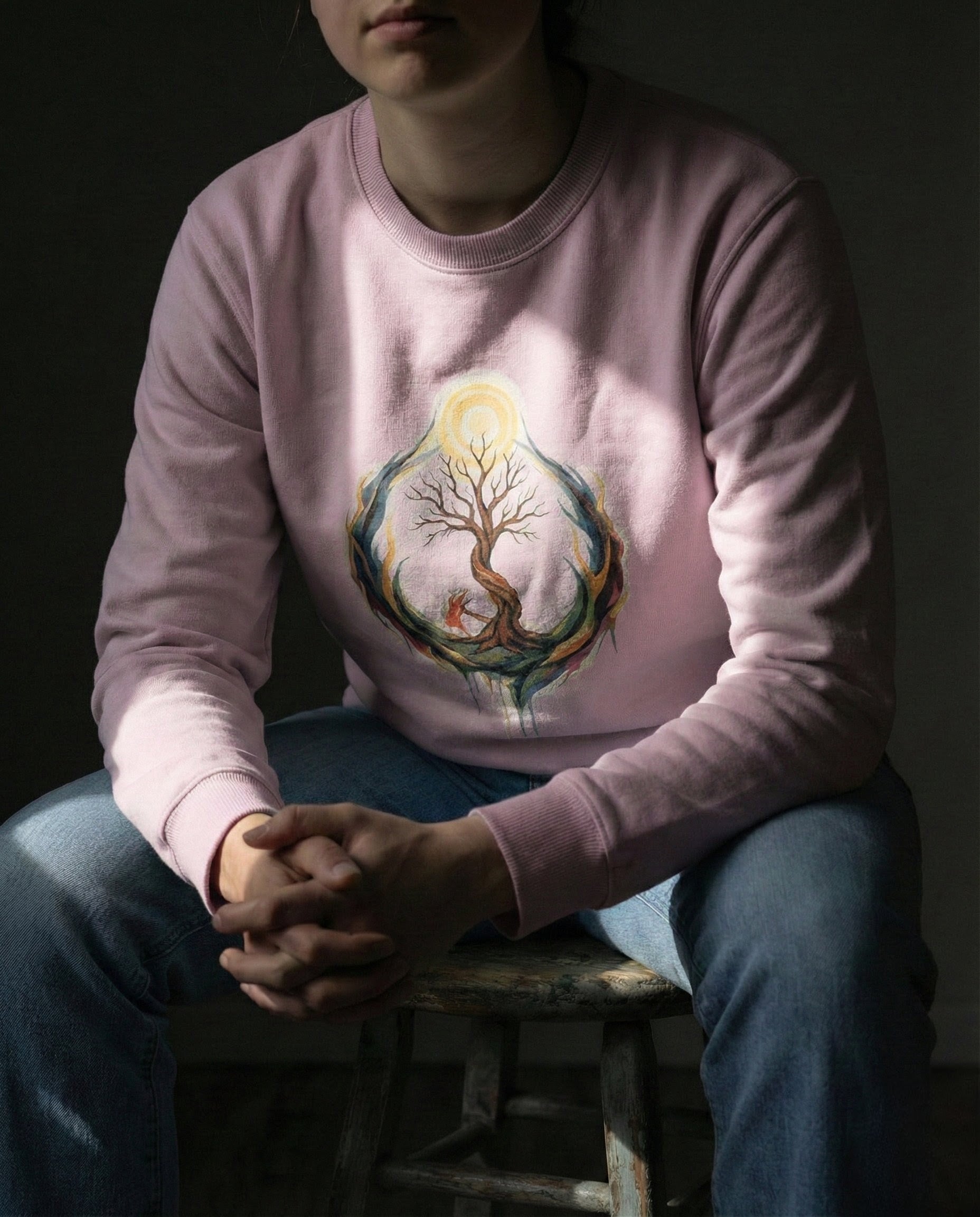 Person wearing a pink sweatshirt with a tree design sitting on a stool against a dark background