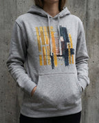 Model wearing the Carbon Grey Tares hoodie, showing gold and dark vertical bars, grid lines and a red spiral.