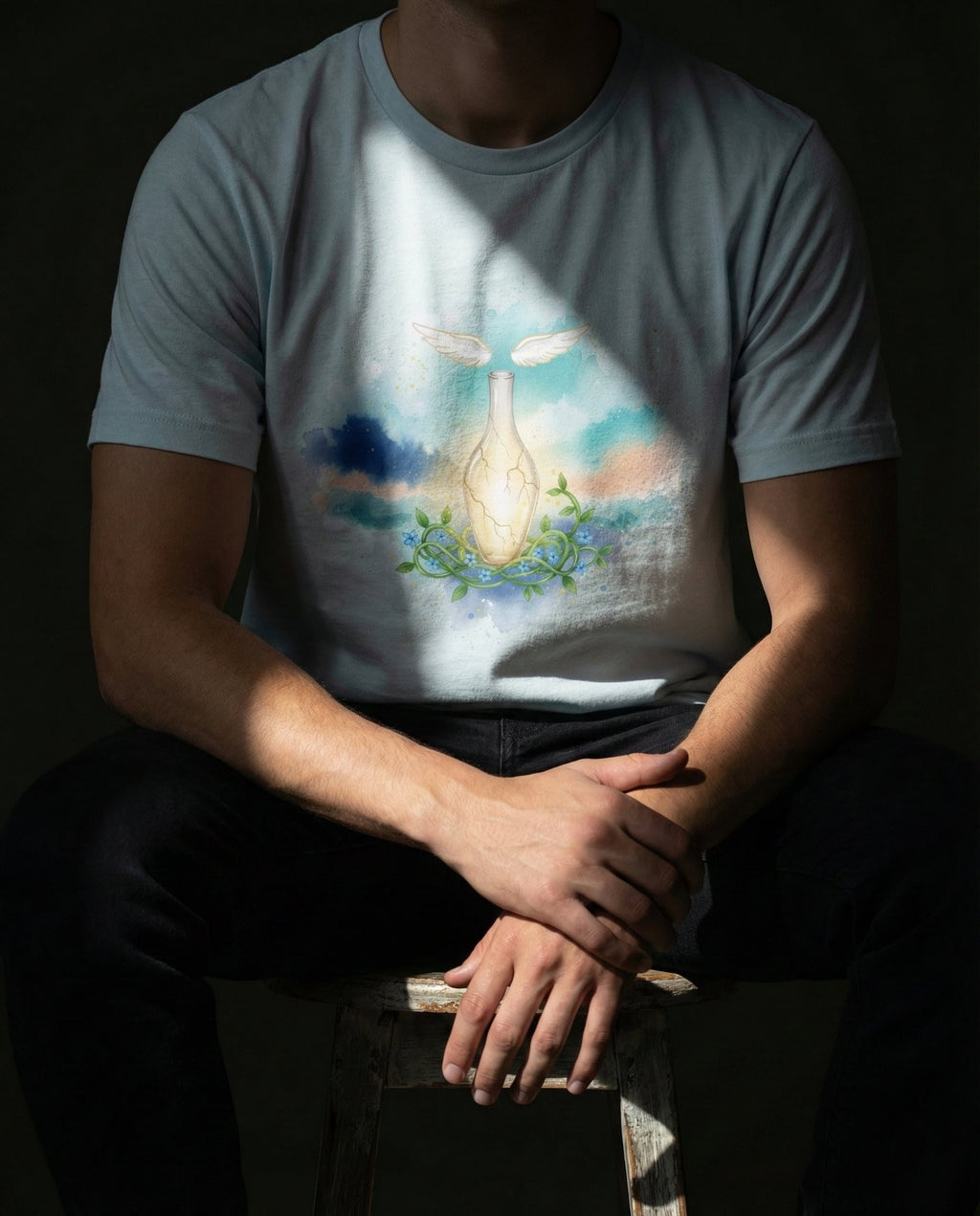 Model wearing a Heather Prism Ice Blue Thorn Tee with a glowing cracked vessel, vines, flowers and wings printed on the front.