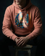 Model wearing a Dusty Rose Separation Hoodie with geometric fish-like forms, dark fragments, a net-like grid and a red dividing line printed on the front.