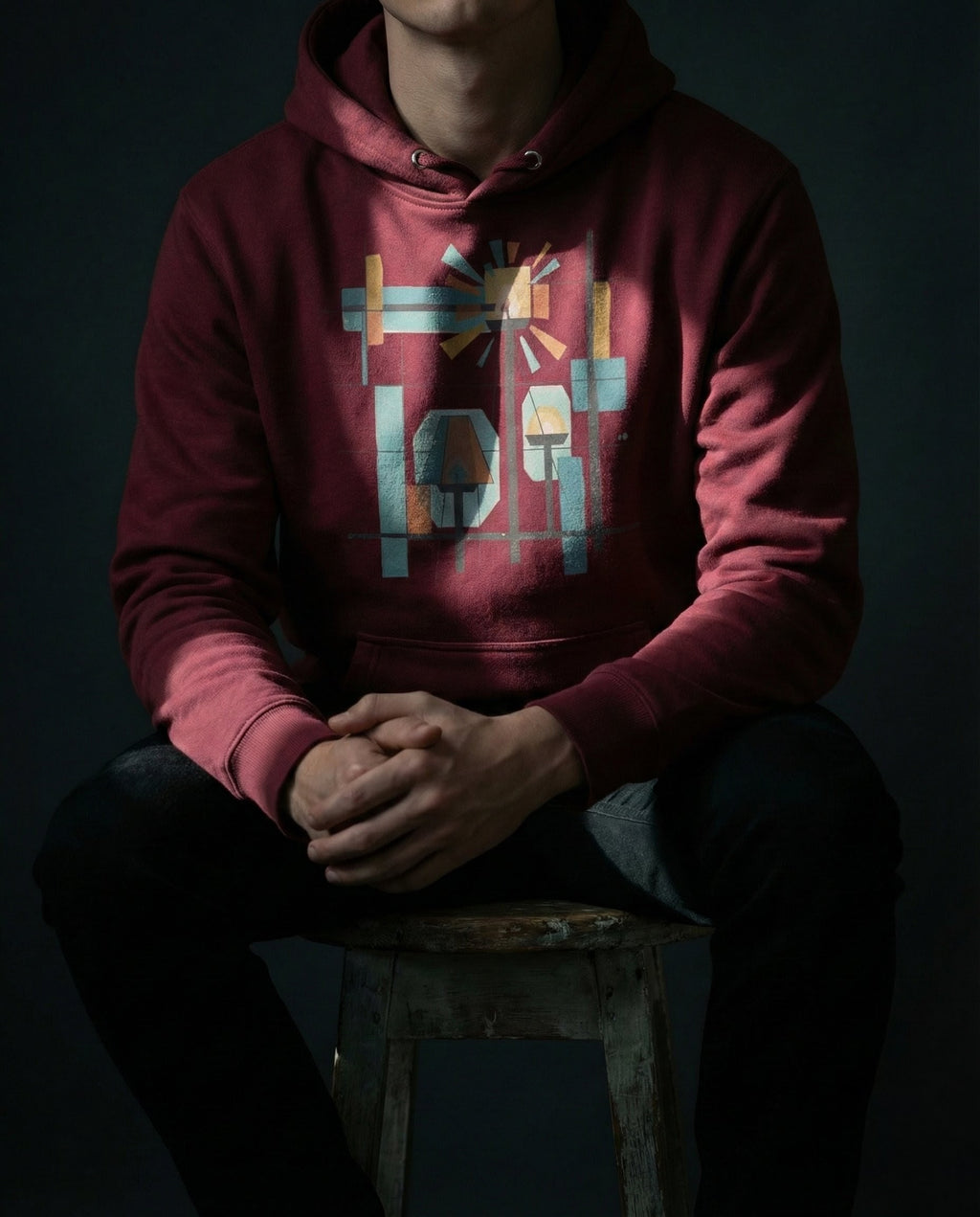 Model wearing the Maroon Bushel Hoodie with geometric lamps, teal and gold rays, colored blocks and a black grid.