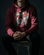 Model wearing the Maroon Bushel Hoodie with geometric lamps, teal and gold rays, colored blocks and a black grid.