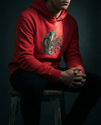 Model wearing a Team Red Cease Striving Hoodie with gold and blue interlocking forms beside scattered black fragments printed on the front.