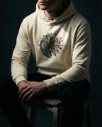Model wearing a Bone Cease Striving Hoodie with gold and blue interlocking forms beside scattered black fragments printed on the front.