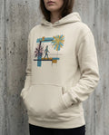 Selah Supply Co. The Foresight Hoodie in Bone. Model in a gritty urban setting wearing a Christian graphic hoodie that visualizes the Parable of the Shrewd Manager (Luke 16). The design features a blindfolded walker on a narrow beam amidst red chaos and a golden starburst.