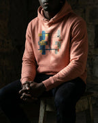 Model wearing the Dusty Rose Lazarus Hoodie with gold, blue, grey and rust geometric artwork.