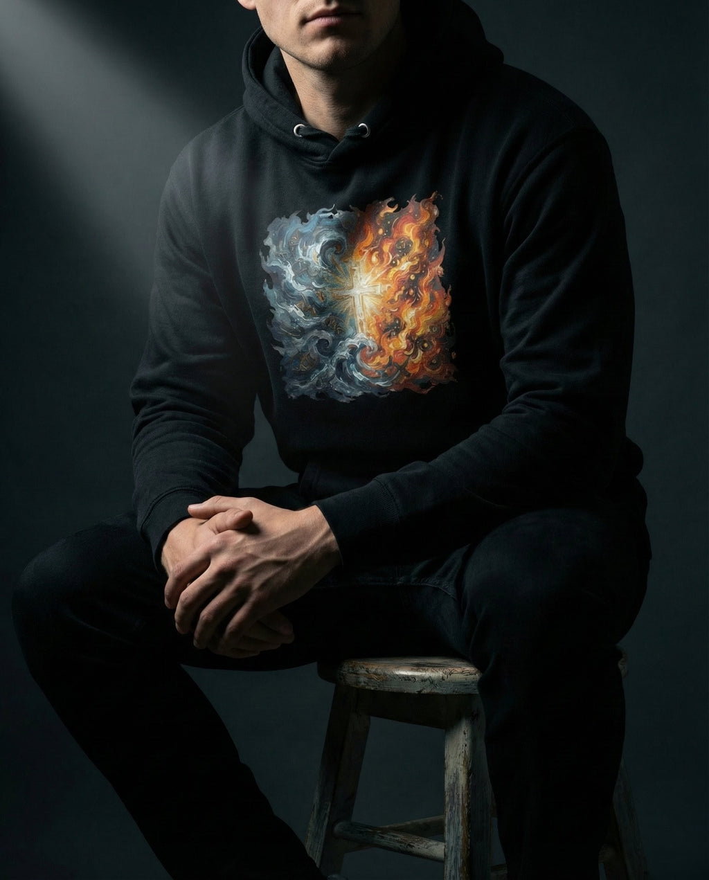 Person wearing a black hoodie with a colorful nebula design, sitting on a stool against a dark background.