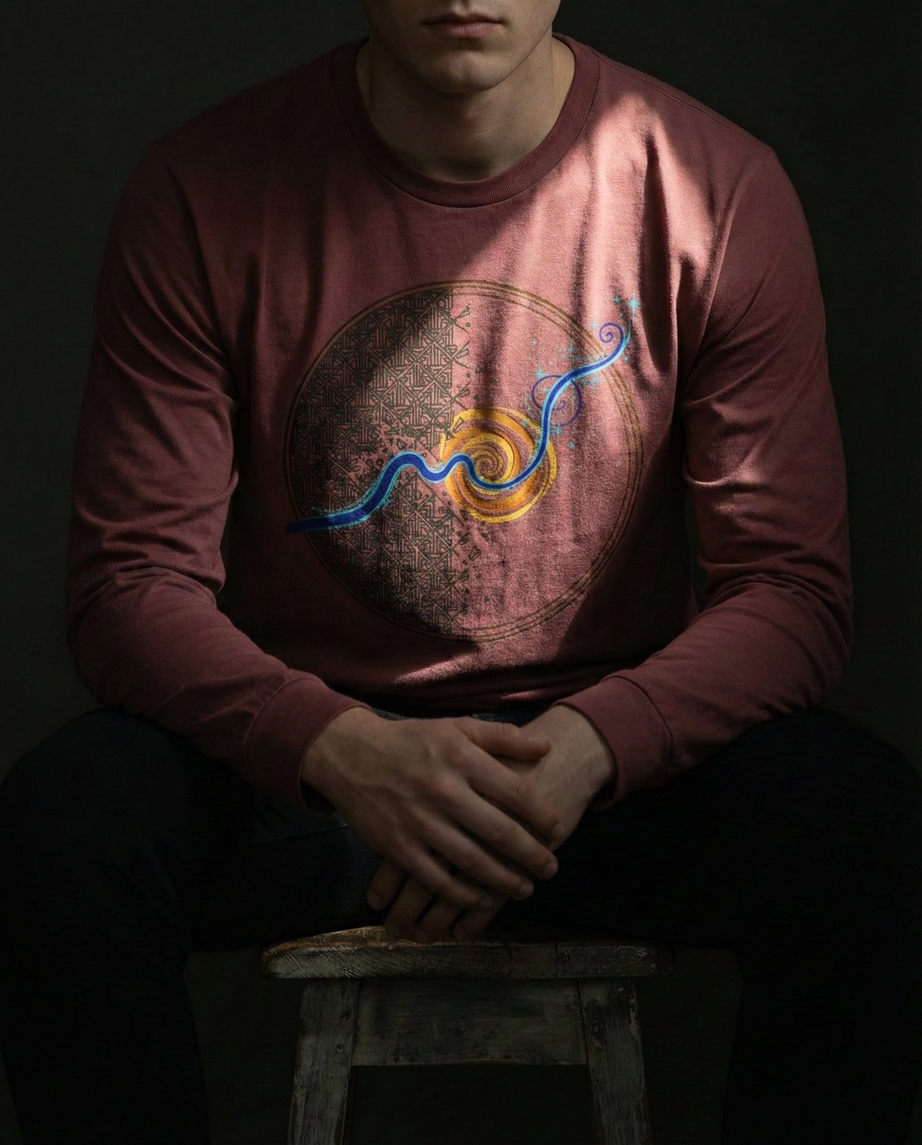 Person wearing a long-sleeve shirt with a graphic design sitting on a stool against a dark background