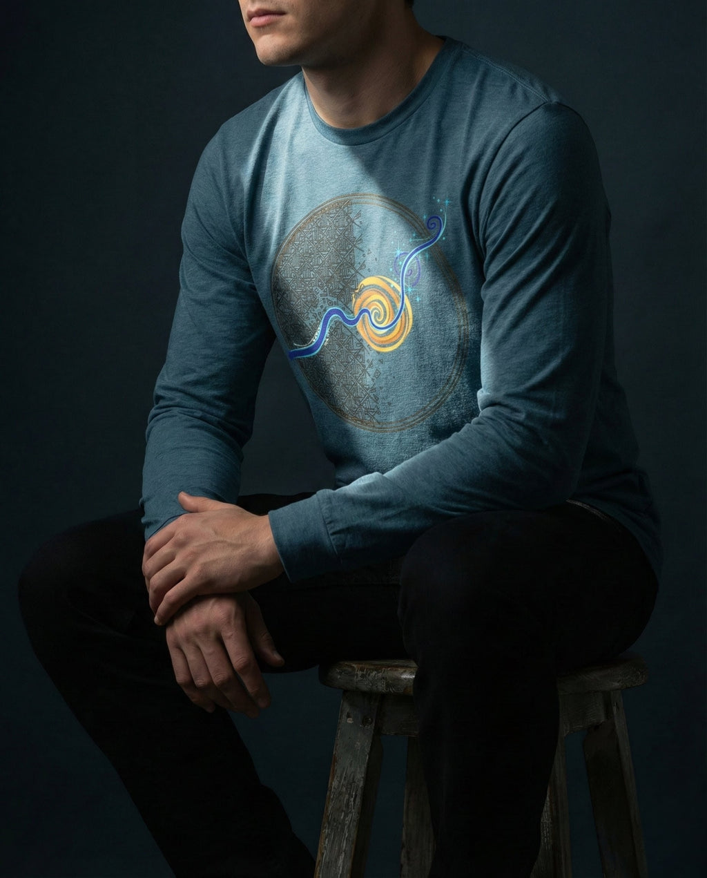 Person wearing a blue long-sleeve shirt with a graphic design, sitting on a dark background