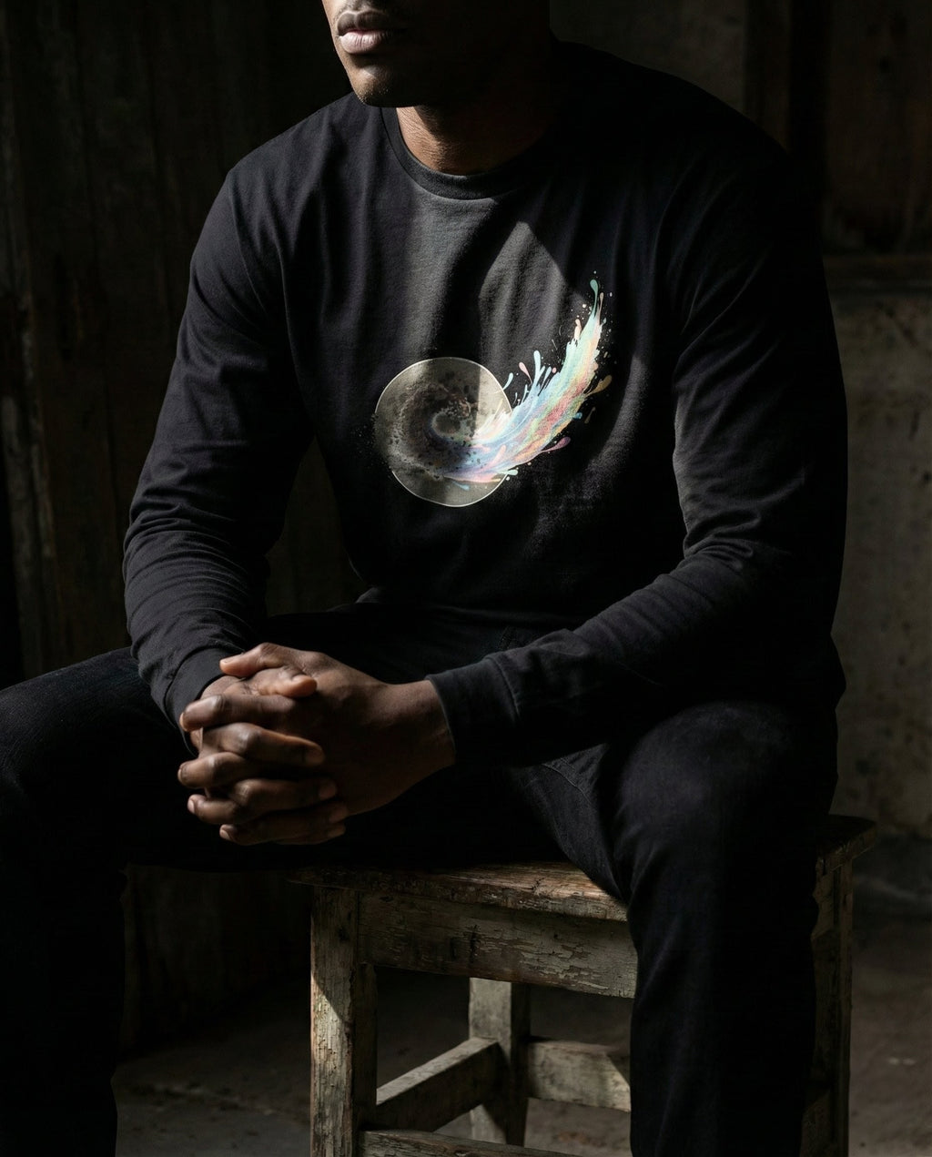 Person wearing a black long-sleeve shirt with a colorful design sitting on a wooden stool.
