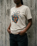 Model wearing the Heather Dust East West Tee with a geometric heart, blue wing-like forms, gold squares and red and black scribbles.