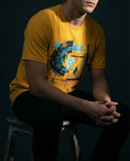 Model wearing the Mustard Ex Nihilo Tee with abstract vortex, red line and geometric grid artwork.