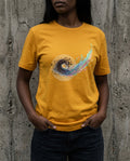 Person wearing a yellow t-shirt with a colorful design against a textured wall.