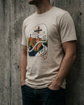 Selah Supply Co. The Lean Not Tee in Soft Cream. Model wearing a Christian graphic tee that visualizes Proverbs 3:5 through an abstract design of hands holding a geometric heart and a path leading to a cross. Styled against a gritty concrete wall.