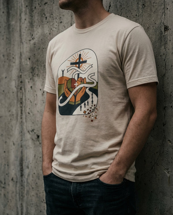 Person wearing a beige t-shirt with a graphic design against a concrete wall.