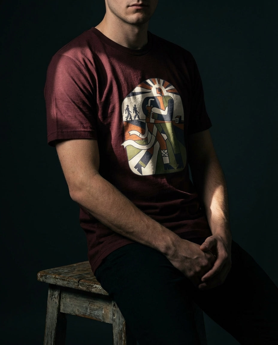 Person wearing a maroon t-shirt with a graphic design, sitting on a wooden stool against a dark background