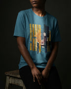 Model wearing the Heather Deep Teal Tares tee, showing gold and dark vertical bars, grid lines and a red spiral.