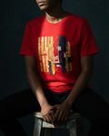 Person wearing a red t-shirt with geometric design sitting on a stool against a dark background