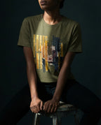 Model wearing the Heather Olive Tares tee, showing gold and dark vertical bars, grid lines and a red spiral.