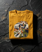 Mustard Two Denarii Tee folded on dark stone, showing a central figure supporting a wounded person, flowing white cloth and smaller walking figures.
