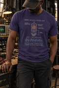 Front view of a standing model in a workshop, wearing a heather blue-purple T-shirt with a vacuum-tube diagram and a voltage waveform graph centered on the front.