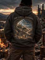 A person viewed from behind wearing a dark charcoal hoodie with a large detailed industrial wasteland graphic on the back and the text 'THE CARMEL BLACKOUT'. The scene is set in a post-apocalyptic wasteland at sunset.