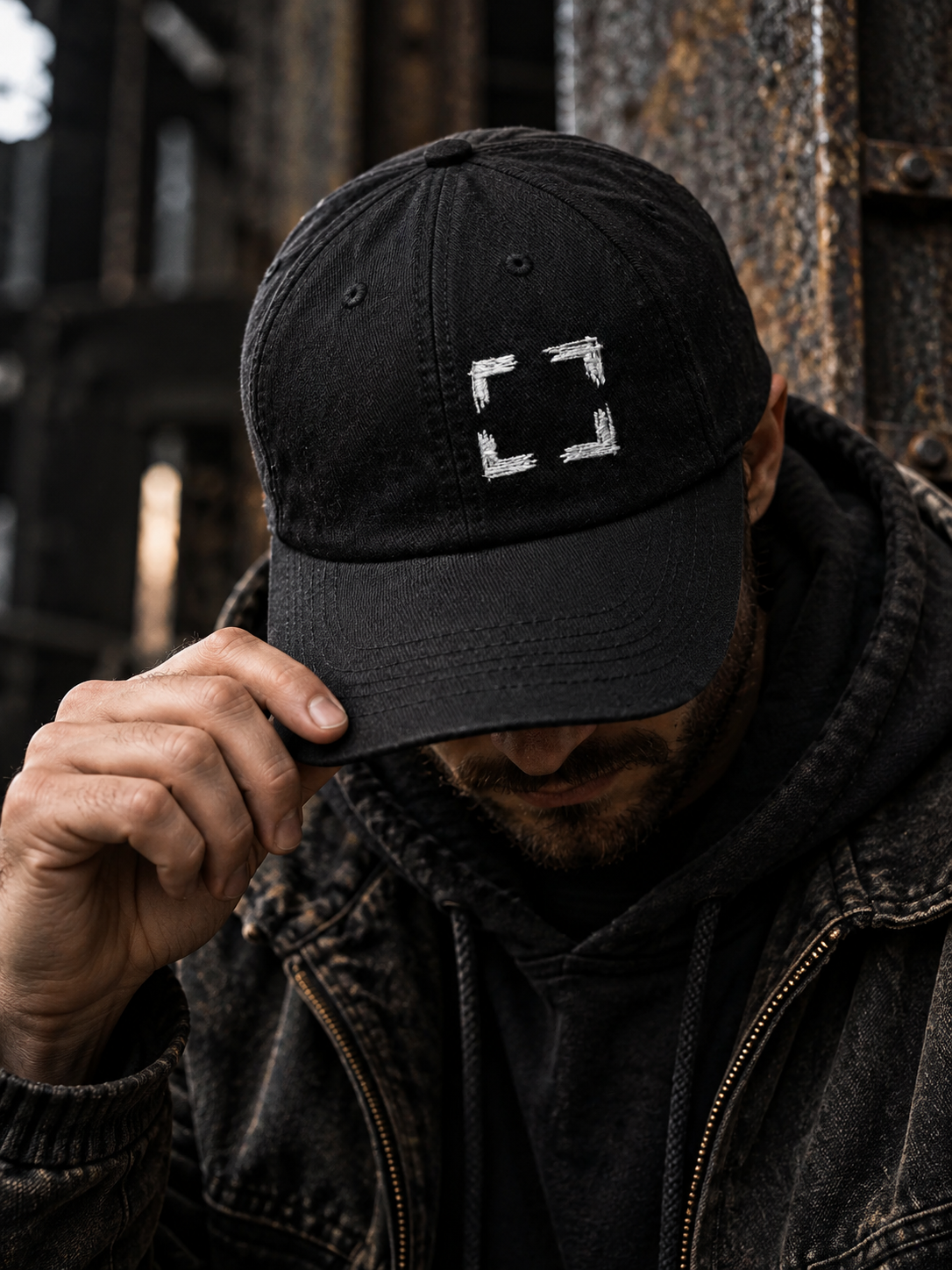 Man holding the brim of a black Cornerstone Hat with four white embroidered corner marks.