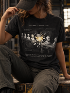 Front view of a seated model in a workshop, wearing a black heather T-shirt with conveyor belts carrying gray busts around a bright yellow burst, overlaid with technical linework centered on the front.