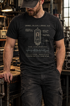 Front view of a standing model in a workshop, wearing a black heather T-shirt with a vacuum-tube diagram and a voltage waveform graph centered on the front.
