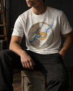 Model wearing the white Rewire tee, with a circular brown grid, blue current and gold spiral, seated on a wooden crate.