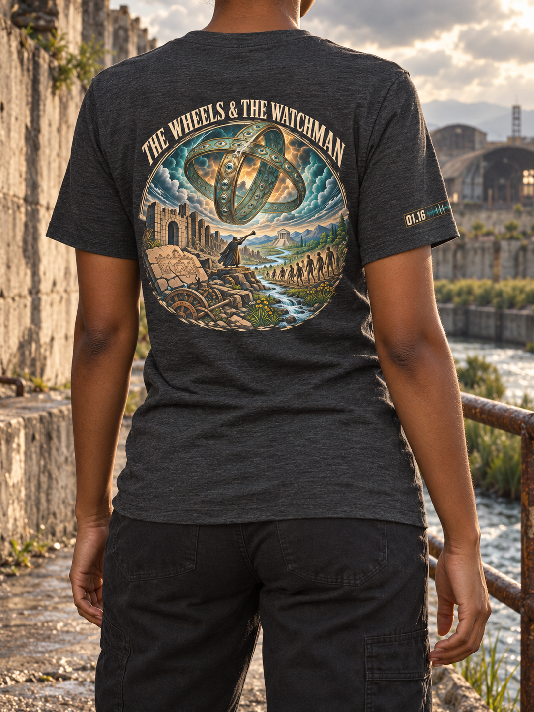 Back view of a charcoal heather T-shirt with THE WHEELS & THE WATCHMAN above interlocking eye-studded rings in clouds, figures, ruins, and a stream.