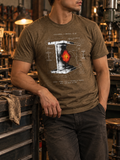 Front view of a standing model in a workshop, wearing a heather brown T-shirt with a white I-beam, a red-orange glowing spot, and technical stress diagrams centered on the front.