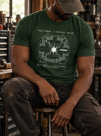 Front view of a seated model in a workshop, wearing a heather emerald T-shirt with a white reaction-chamber schematic surrounding a bright central spark centered on the front.