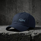 Navy Sand Sketch Cap with light fish embroidery on concrete.
