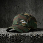 Green camo Sand Sketch Cap with light fish embroidery on concrete.